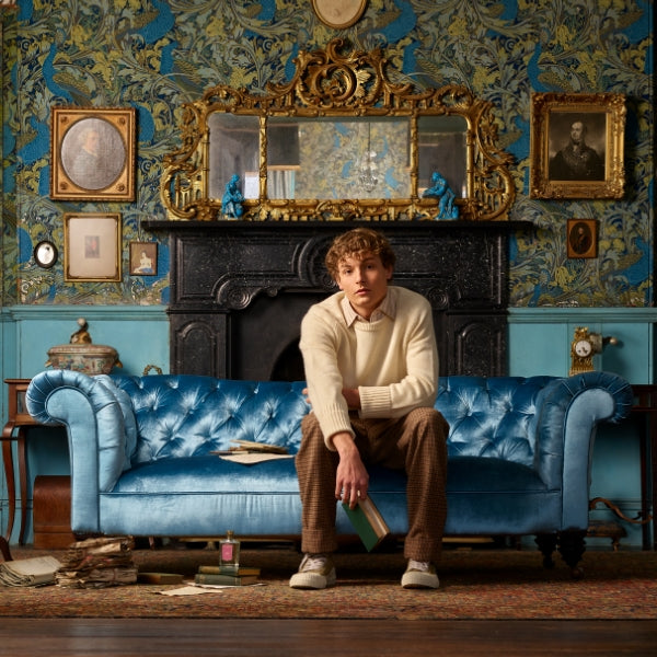 Floris - Wilde Szenische Aufnahme mit blauem Samtsofa, historischem Interieur und Mann mit Buch auf klassischem Teppich