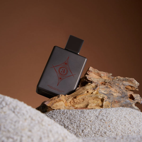 Spiritum - 3 - Wisdom Universe Parfumflakon in dunklem Design mit rotem Symbol auf Holzstück vor braunem Hintergrund