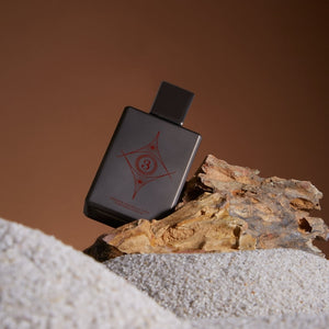 Spiritum - 3 - Wisdom Universe Parfumflakon in dunklem Design mit rotem Symbol auf Holzstück vor braunem Hintergrund