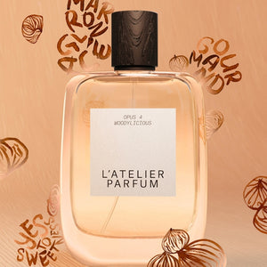 L'Atelier Parfum - Opus 4 - Woddylicious Flakon mit schwarzem Holzverschluss vor hellem Hintergrund mit Marron-Illustrationen