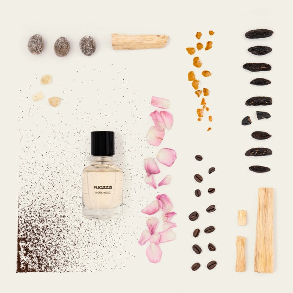 Fugazzi - Workaholic mit klarem Flakon, umgeben von Kaffee, Rosenblättern, Holz und weiteren natürlichen Duftnoten vor hellem Hintergrund